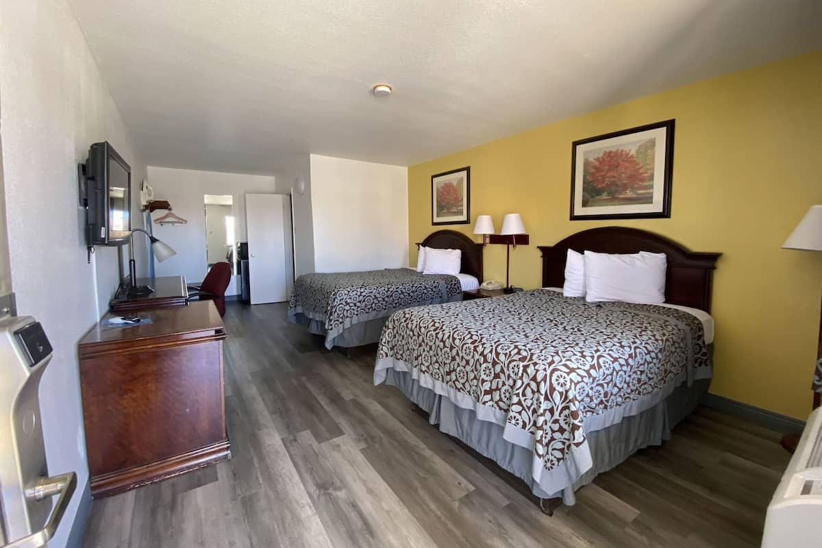 A hotel room with two beds, a desk, a TV, and a door leading to another room.