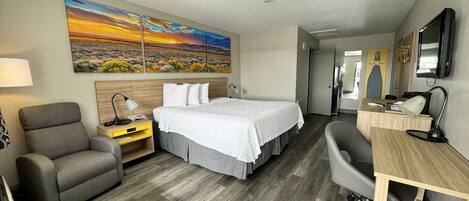 Quarto de hotel com cama, escrivaninha, cadeira e uma pintura de uma paisagem ao pôr do sol.