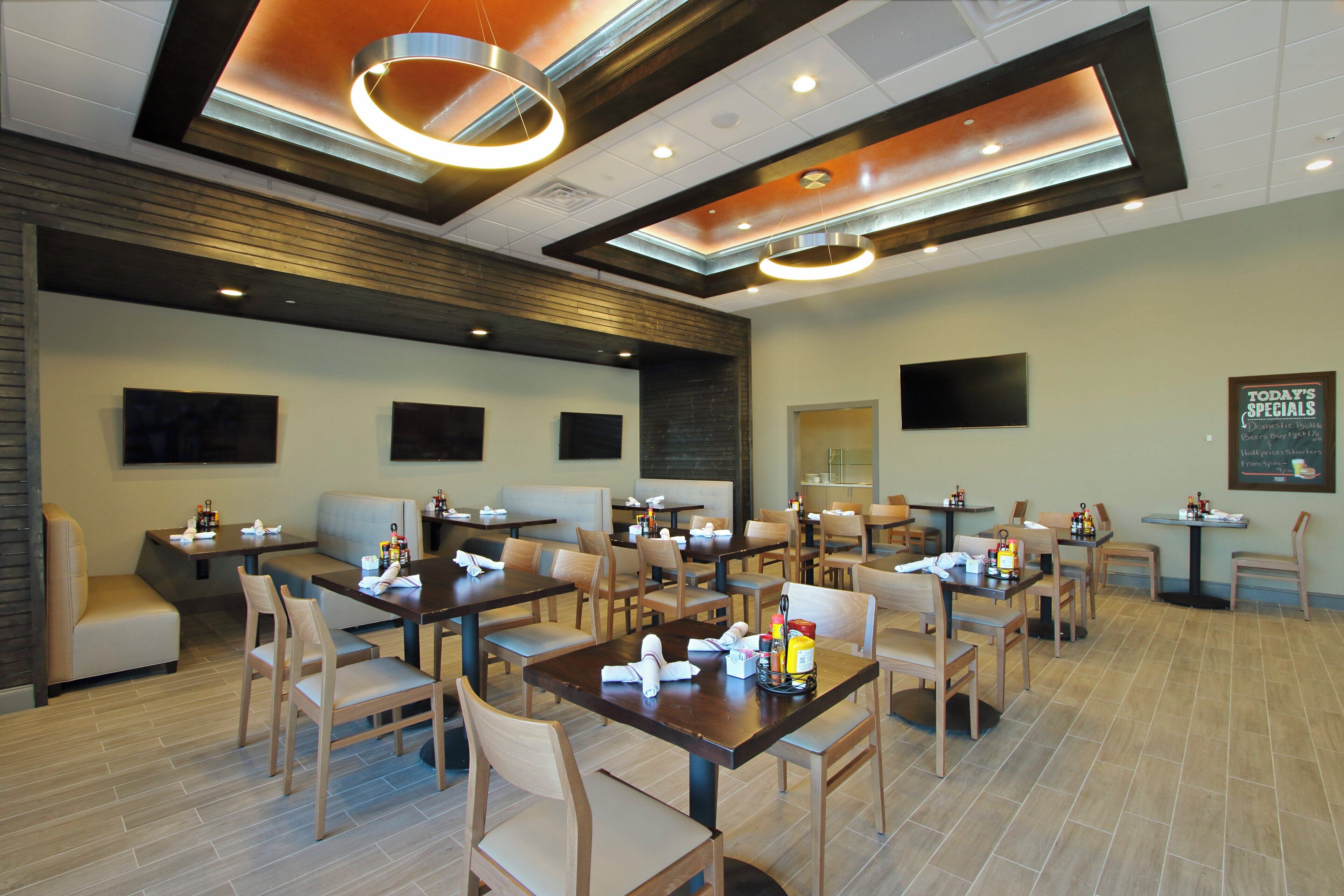Un restaurante con varias mesas y cabinas, luces en el techo y una pizarra con el menú.
