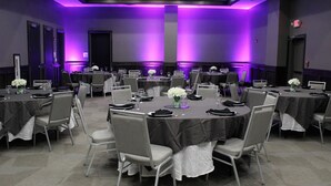 Un salón de conferencias con varias mesas y sillas, iluminación ambiental morada y una pantalla de proyector.