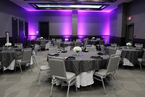 Un salón de conferencias con varias mesas y sillas, iluminación ambiental morada y una pantalla de proyector.