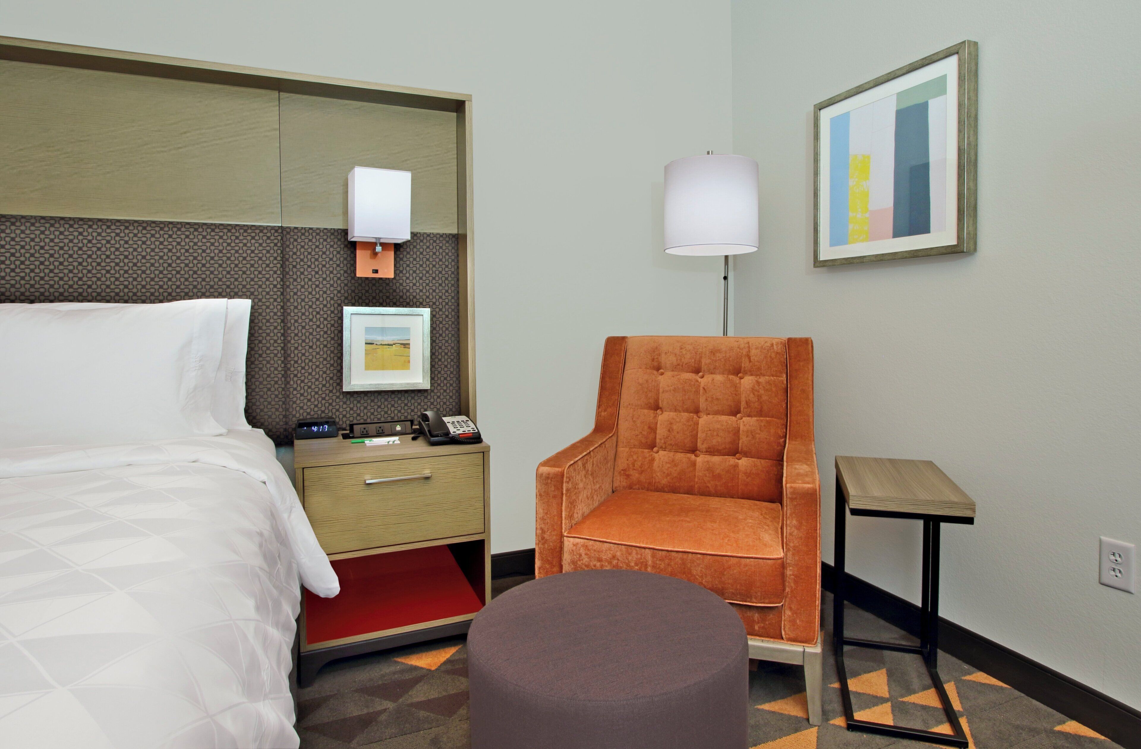 Una camera d'hotel con un letto, una scrivania con il telefono, una sedia, una lampada e un quadro appeso al muro.