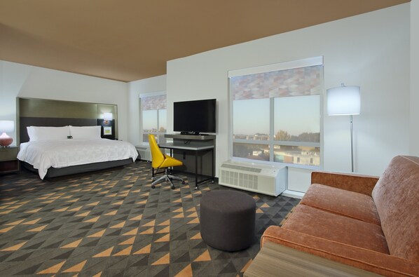 Hotelkamer met een bed, bureau, televisie, bank en een groot raam met uitzicht op de stad.