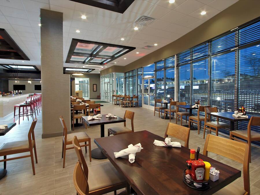 A spacious restaurant with multiple dining tables and chairs, large windows offering a view of the outside, and a modern ceiling design.