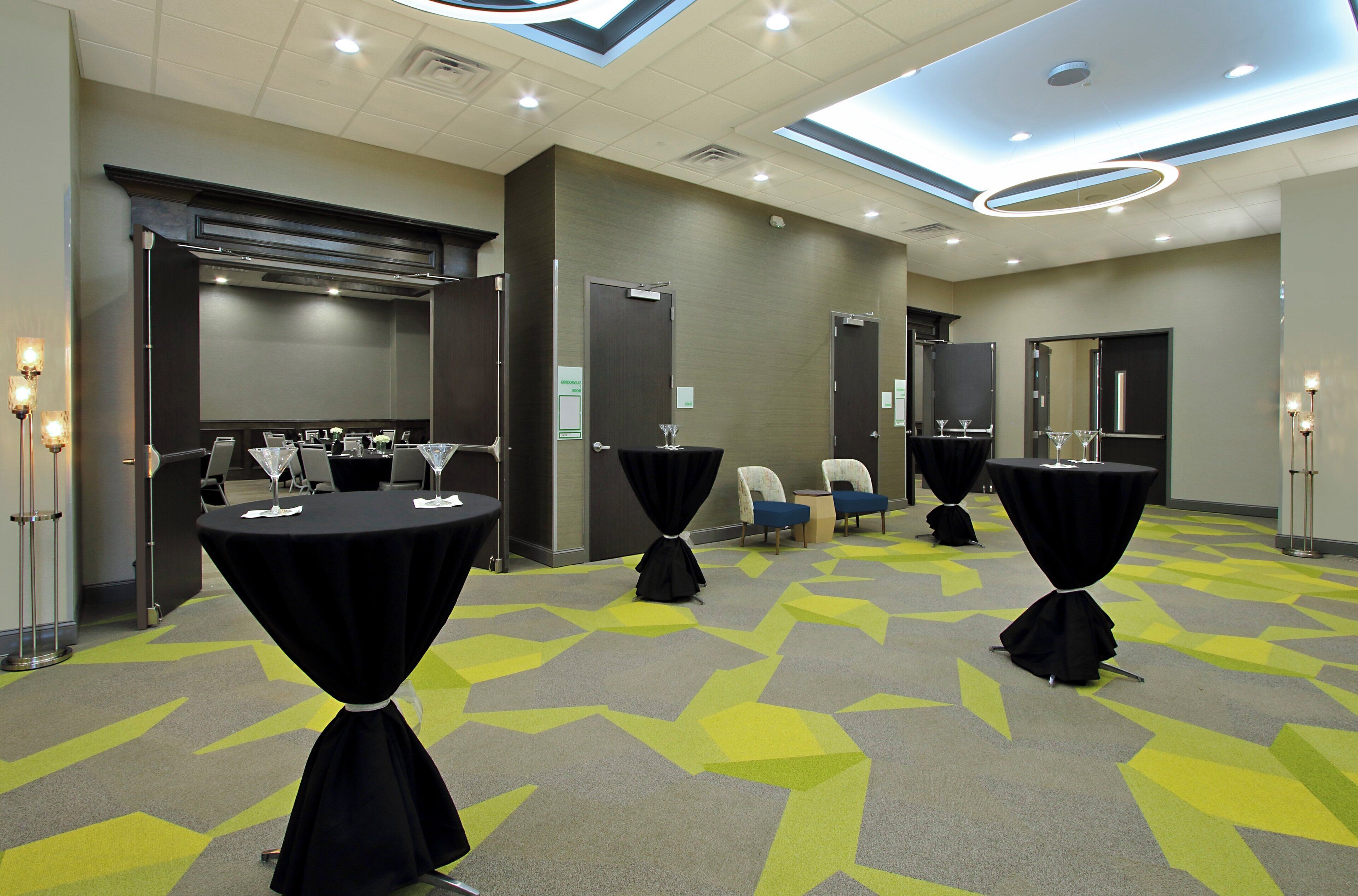 Un salón de conferencias con mesas dispuestas para una reunión, equipado con sillas y una pantalla de proyector.