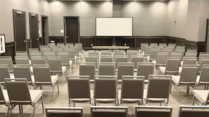 Un salón de conferencias con filas de sillas, una pantalla de proyección y una puerta.