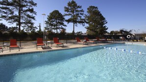 Una piscina con sillas de descanso rojas y altos árboles al fondo.