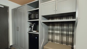 Una cocina compacta con armarios grises, un microondas, un refrigerador pequeño y un banco con estampado escocés.