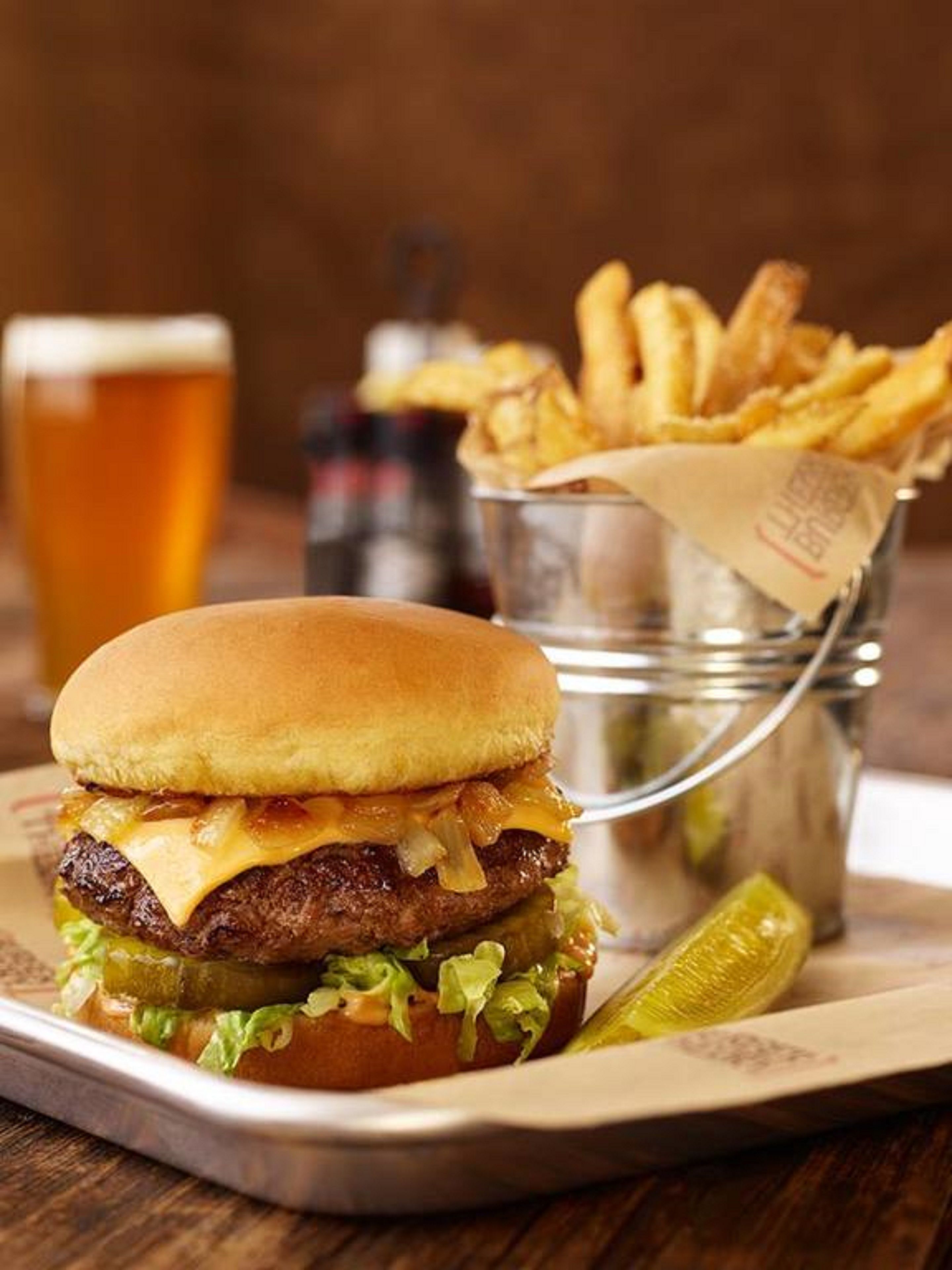 A burger with fries and a pickle on a wooden table.