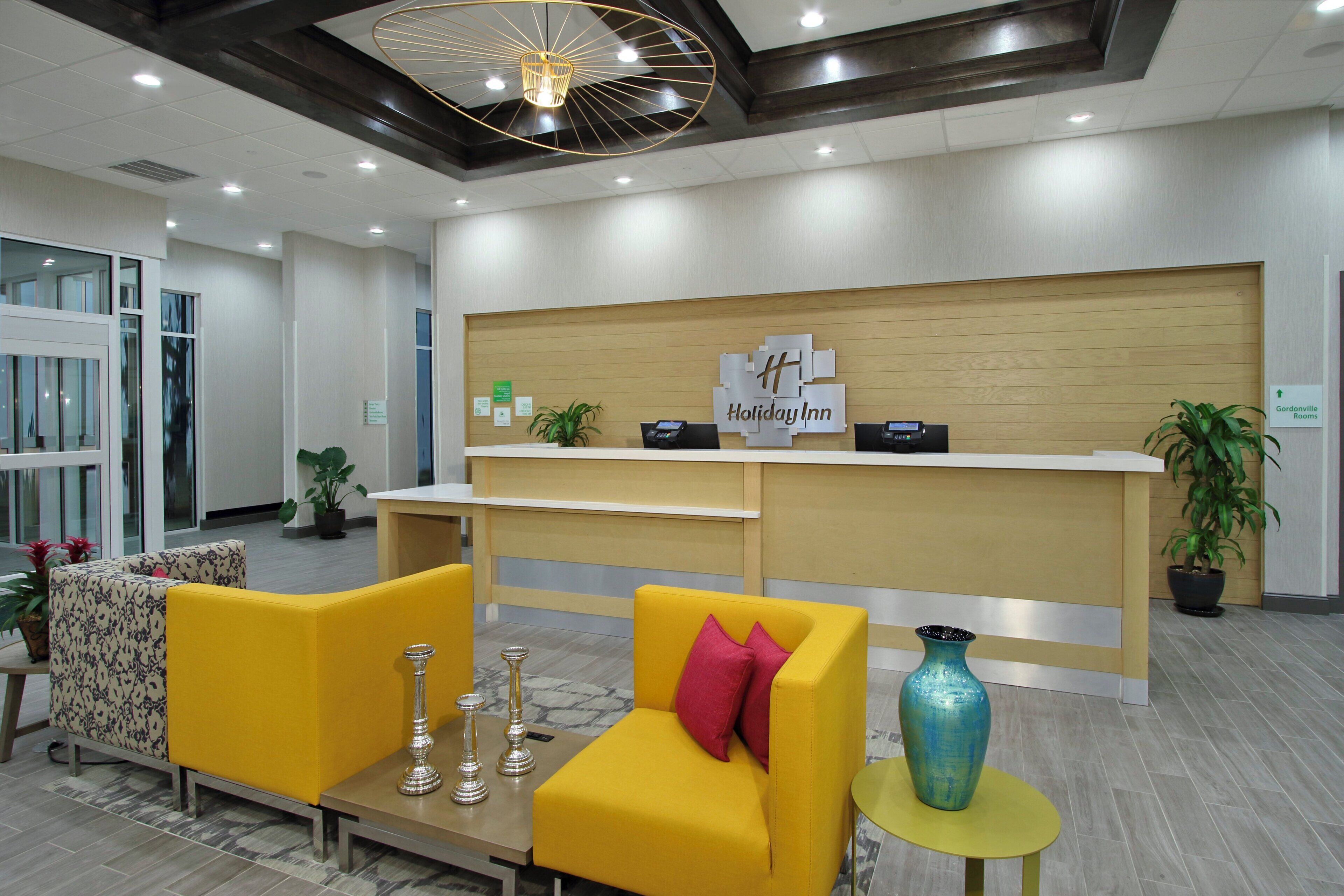 Zona de recepción de hotel con diseño moderno, que incluye mostrador de recepción, área de estar y elementos decorativos.
