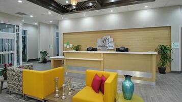 Zona de recepción de hotel con diseño moderno, que incluye mostrador de recepción, área de estar y elementos decorativos.