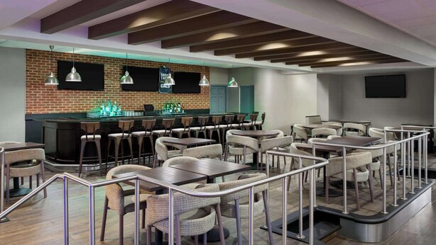 Een modern restaurant met een bakstenen muur, een bar en meerdere eettafels met stoelen.