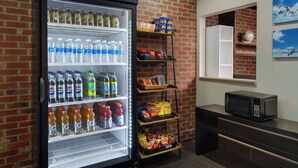 Een automaat gevuld met drankjes en snacks, een magnetron, en een bakstenen muur.
