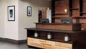 Een receptiebalie met een bakstenen muur, ingelijste foto's aan de muur en een koffiehoek met twee koffiezetapparaten.