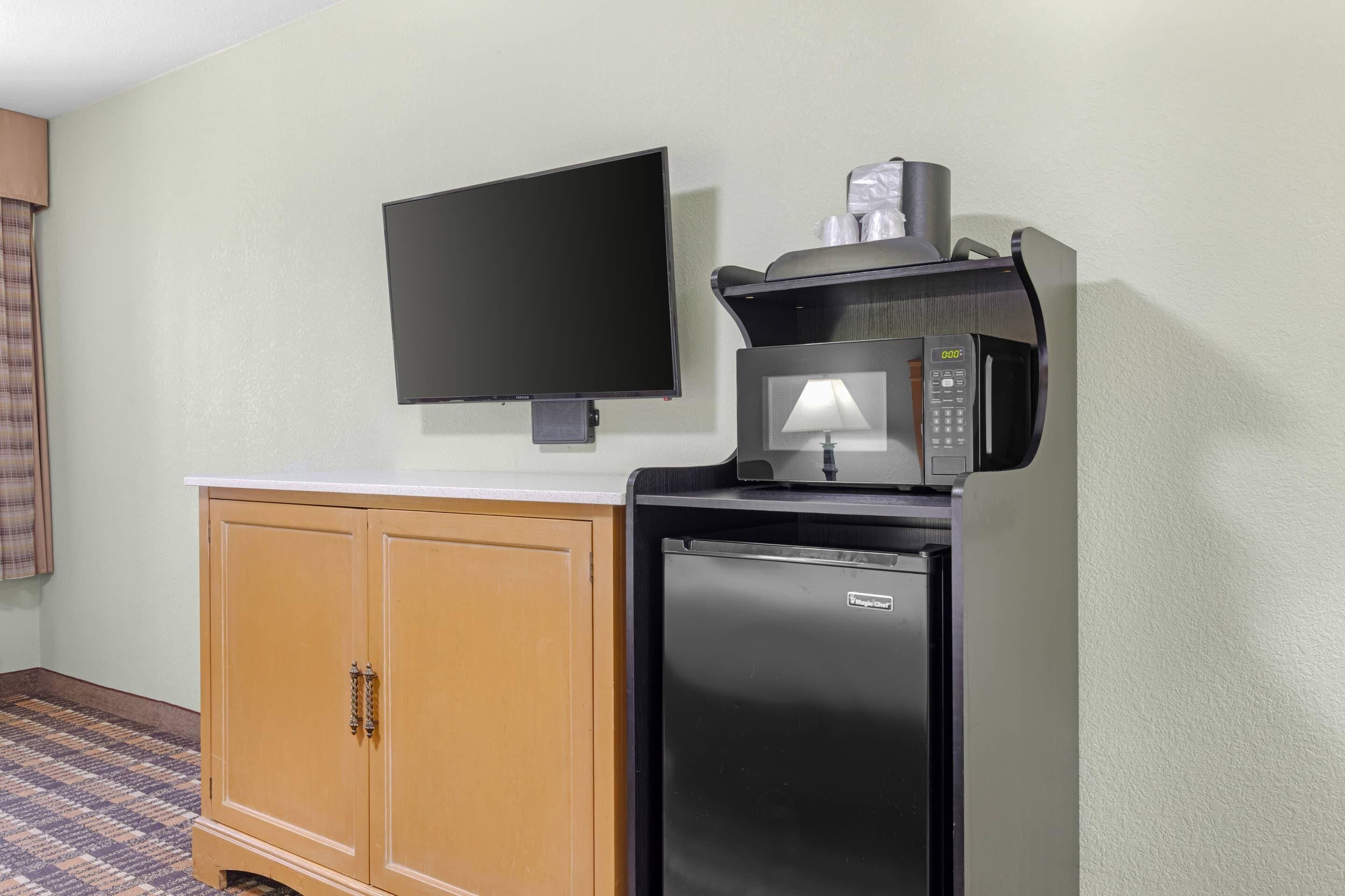 Una kitchenette equipada con microondas, refrigerador y televisor de pantalla plana montado en la pared.