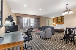 A hotel room with a desk, two chairs, a sofa, a dining table, and a chandelier. - Quality Inn & Suites Plano East - Richardson (Plano)