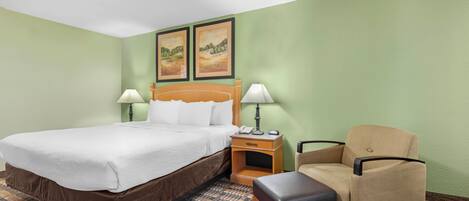 A hotel room with a bed, two bedside lamps, a chair, a small table, and two framed pictures on the wall.