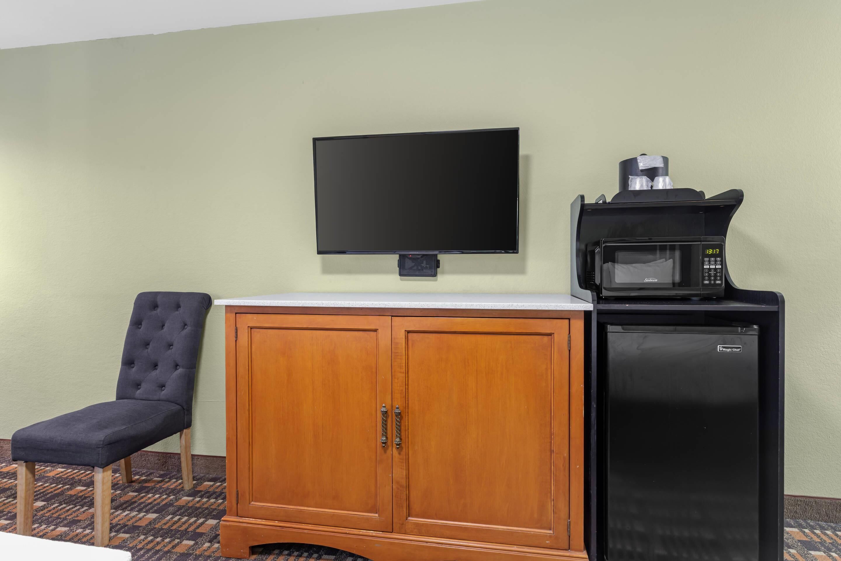 A hotel room with a television, a minibar, a microwave, and a cushioned chair.