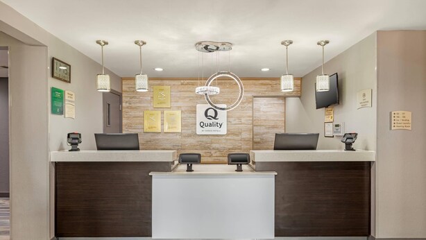 A hotel reception area with a modern design, featuring a reception desk, digital monitors, and a sign indicating the hotel name. - Quality Inn & Suites Plano East - Richardson (Plano)