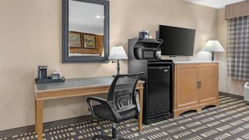 A hotel room with a desk, chair, television, refrigerator, and a patterned floor.