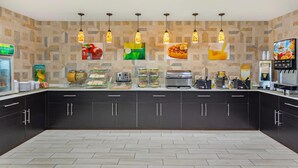 A modern kitchen with dark cabinets, a countertop with various appliances, and hanging pendant lights. - Quality Inn & Suites Plano East - Richardson (Plano)