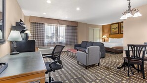 A hotel room with a bed, a sofa, a desk with a lamp, a chair, and a patterned carpet. - Quality Inn & Suites Plano East - Richardson (Plano)