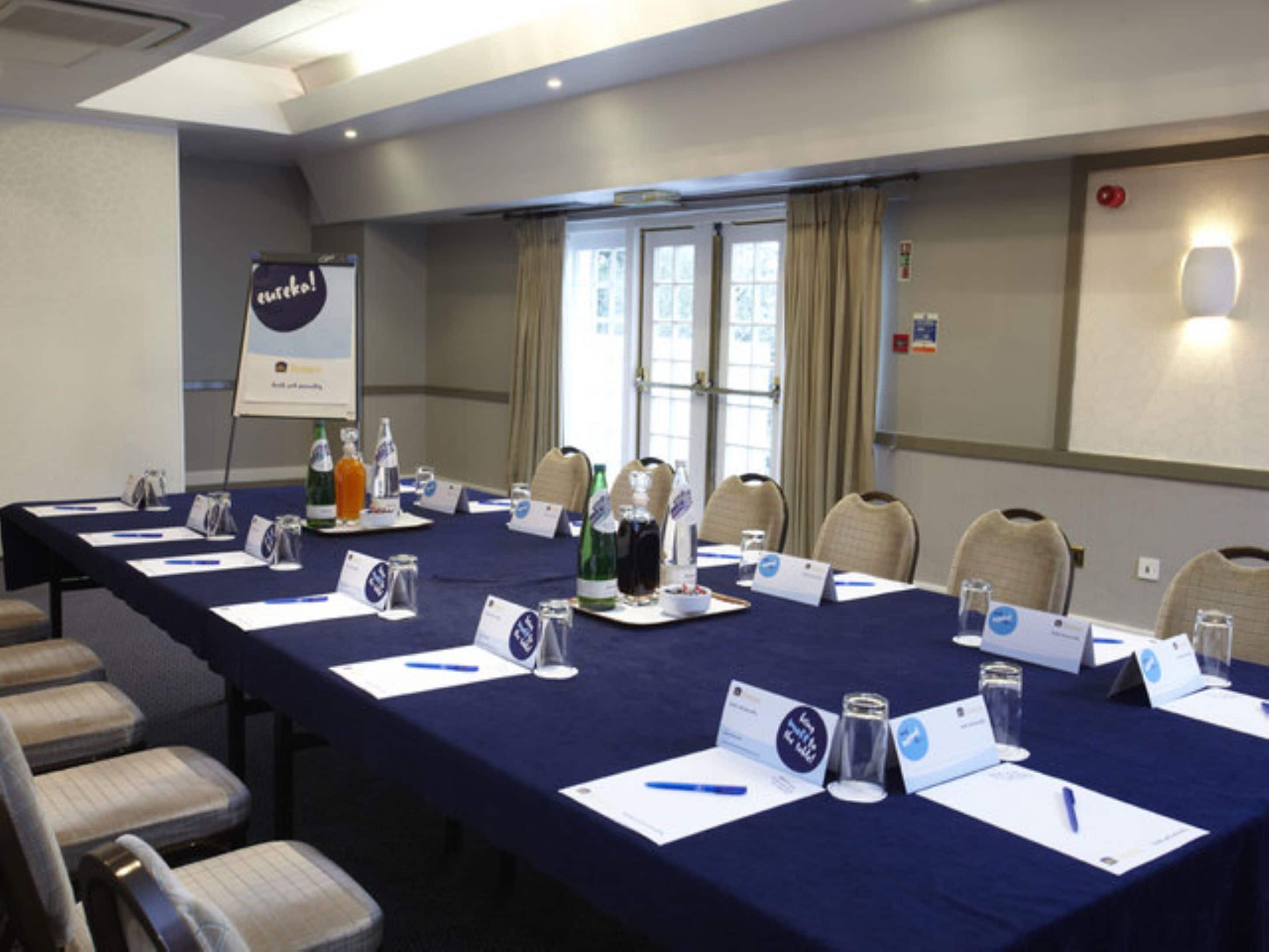 Un salón de conferencias con una larga mesa, tarjetas de identificación, botellas de agua y sillas.