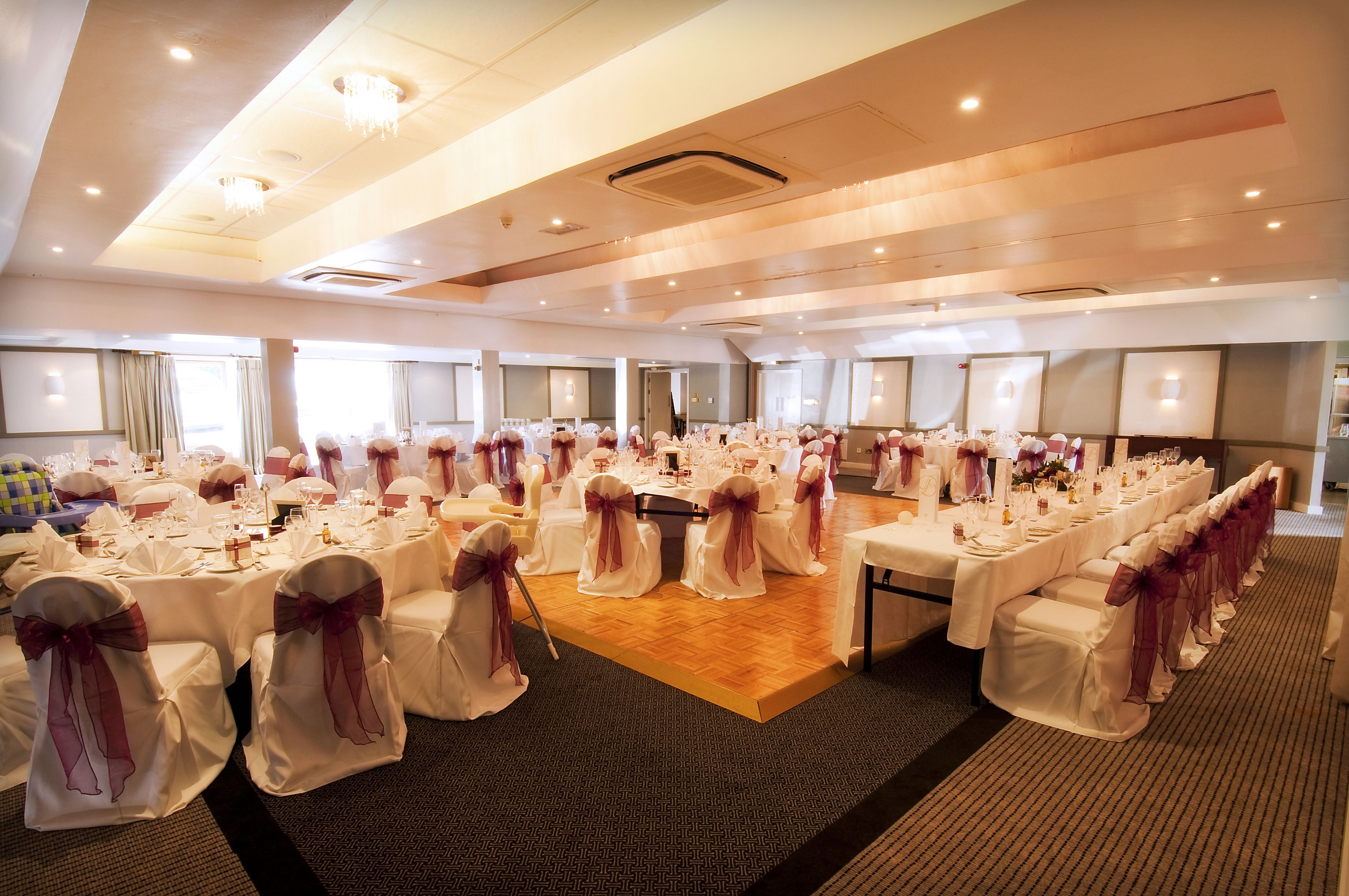 Une salle de banquet avec des tables rondes, des nappes blanches et des chaises ornées de rubans violets.