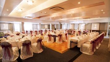 Une salle de banquet avec des tables rondes, des nappes blanches et des chaises ornées de rubans violets.