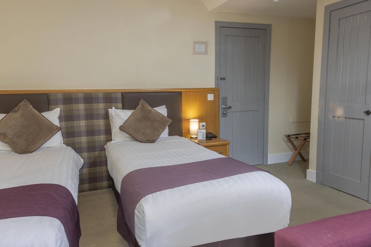 Une chambre d’hôtel avec deux lits, une table de chevet, une lampe et une porte.