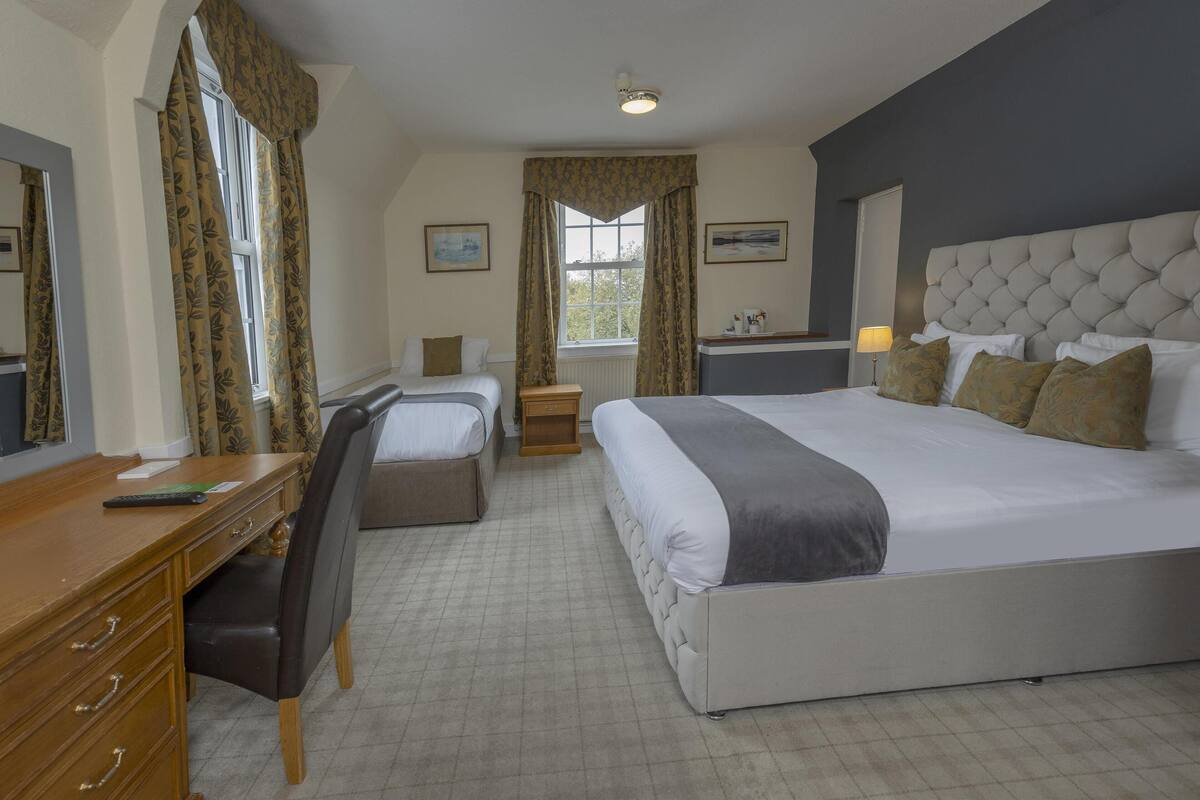 Une chambre d’hôtel avec un grand lit, un bureau avec une chaise, une table de chevet et une fenêtre avec des rideaux.