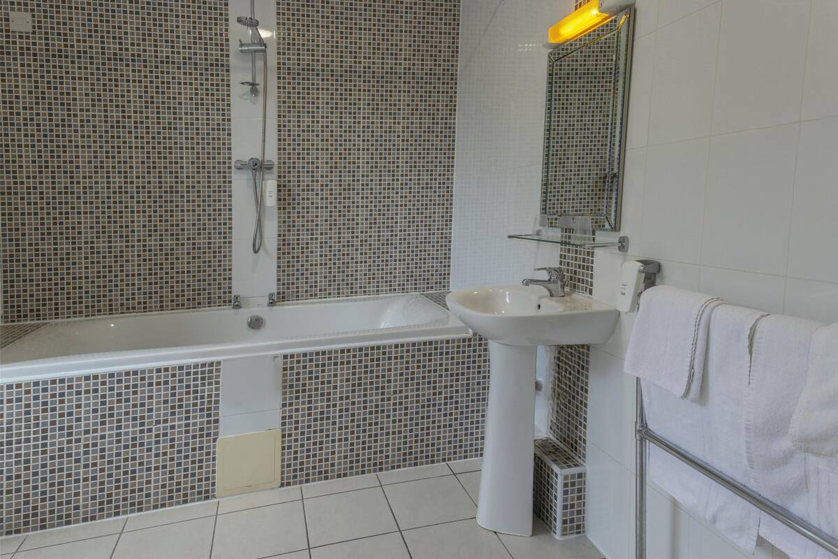 Une salle de bain avec une paroi de douche carrelée, une baignoire, un lavabo et un miroir.