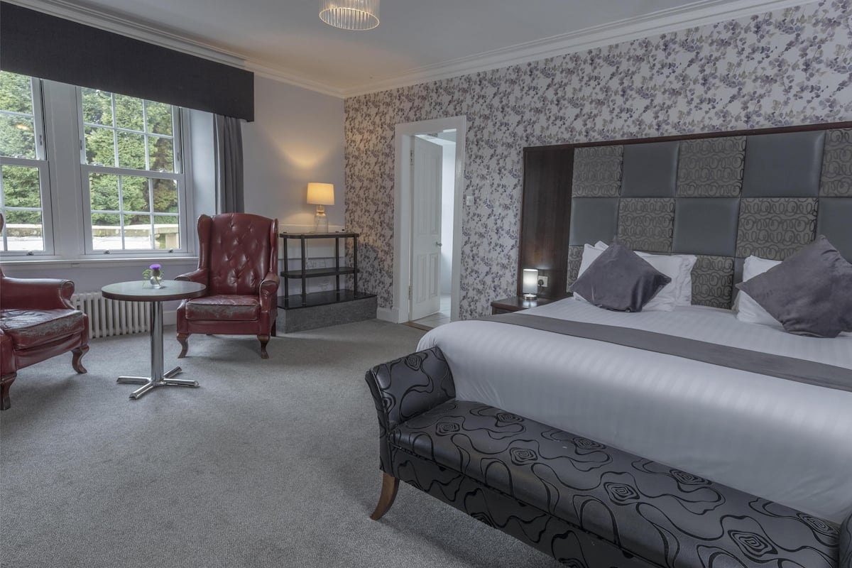 Une chambre d’hôtel avec un grand lit, un bureau, deux fauteuils, une petite table et un banc.