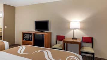 Ein Hotelzimmer mit einem Bett, einem Schreibtisch mit Lampe, einem Fernseher, einer Mikrowelle und zwei Stühlen.