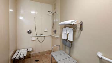 Un baño pequeño y bien iluminado con ducha, inodoro, barra de apoyo, banco y toallero.