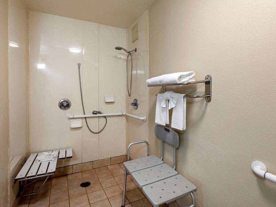 Un baño pequeño y bien iluminado con ducha, inodoro, barra de apoyo, banco y toallero.