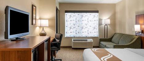 Une chambre d’hôtel comprenant un lit, un bureau avec une télévision, une chaise, un canapé, deux lampes et un appareil de climatisation.