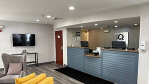 A reception area with a flat-screen TV, a reception desk, a chair, and a yellow sofa. - Quality Inn Placentia Anaheim Fullerton (Placentia)
