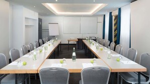 A conference room with a long table, chairs, a whiteboard, and a projector. - ibis Styles Cologne Airport Troisdorf (Troisdorf)