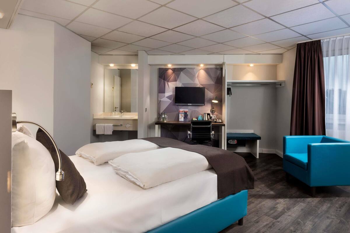 Hotellihuone, jossa on sänky, työpöytä, televisio ja tuoli.