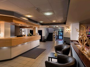 Ein Empfangsbereich mit Rezeptionstheke, einer Treppe und einer Sitzecke mit Stühlen und Tisch.