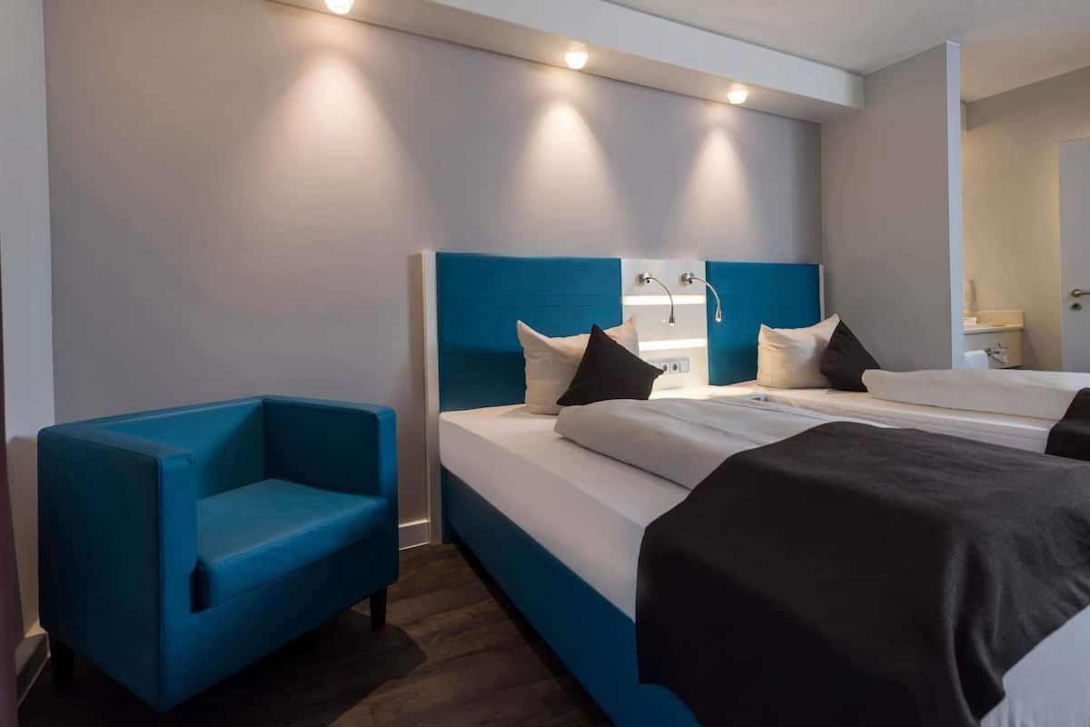 Hotellihuone, jossa on sänky, sininen nojatuoli ja yöpöytä, jossa on peili.