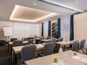 A conference room with tables, chairs, a whiteboard, and a digital display.