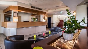 A reception area with a wooden reception desk, a black leather sofa, and a coffee table with candles. - ibis Styles Cologne Airport Troisdorf (Troisdorf)