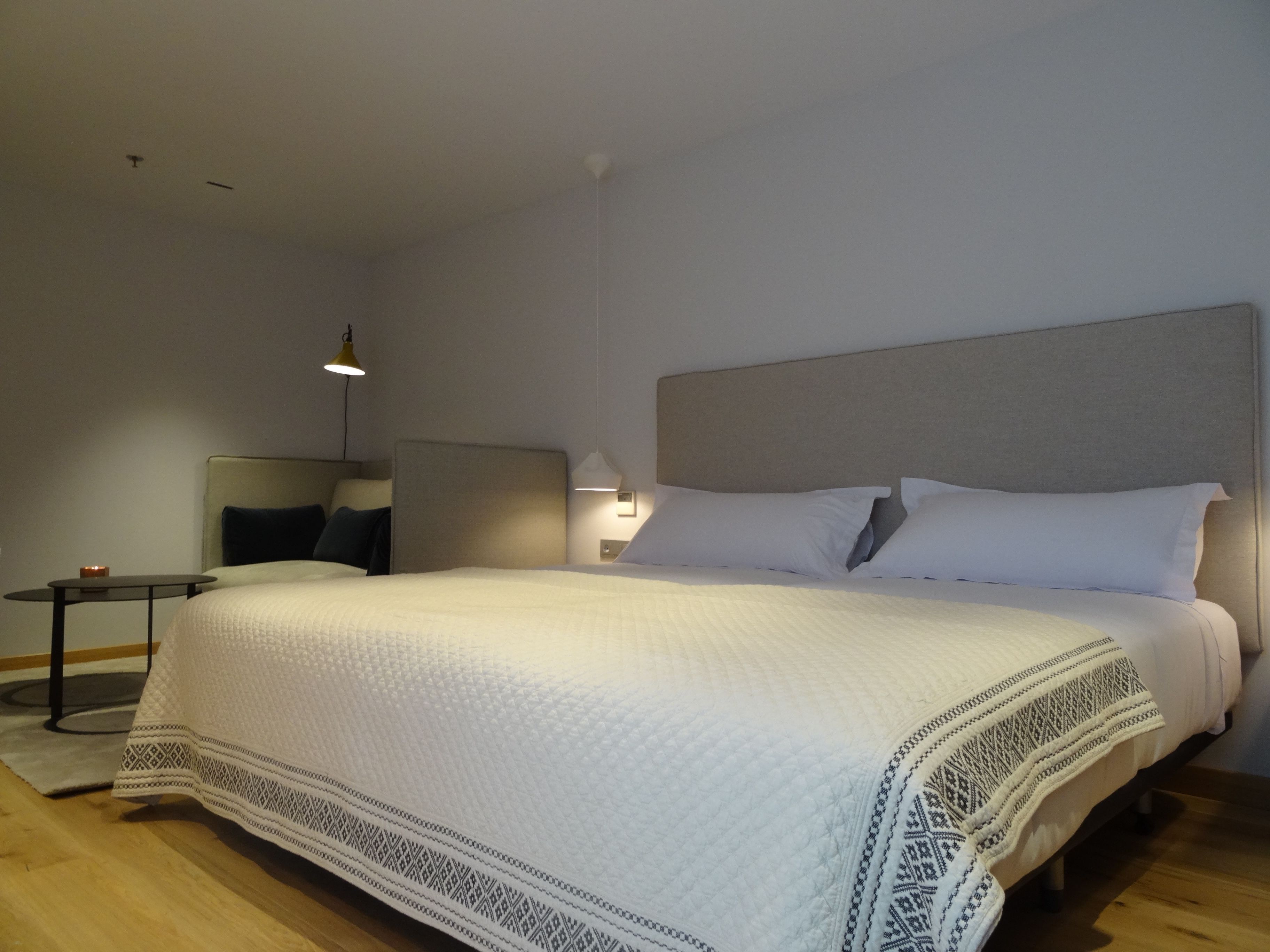 A modern hotel room with a large bed, a bedside table, and a lamp.