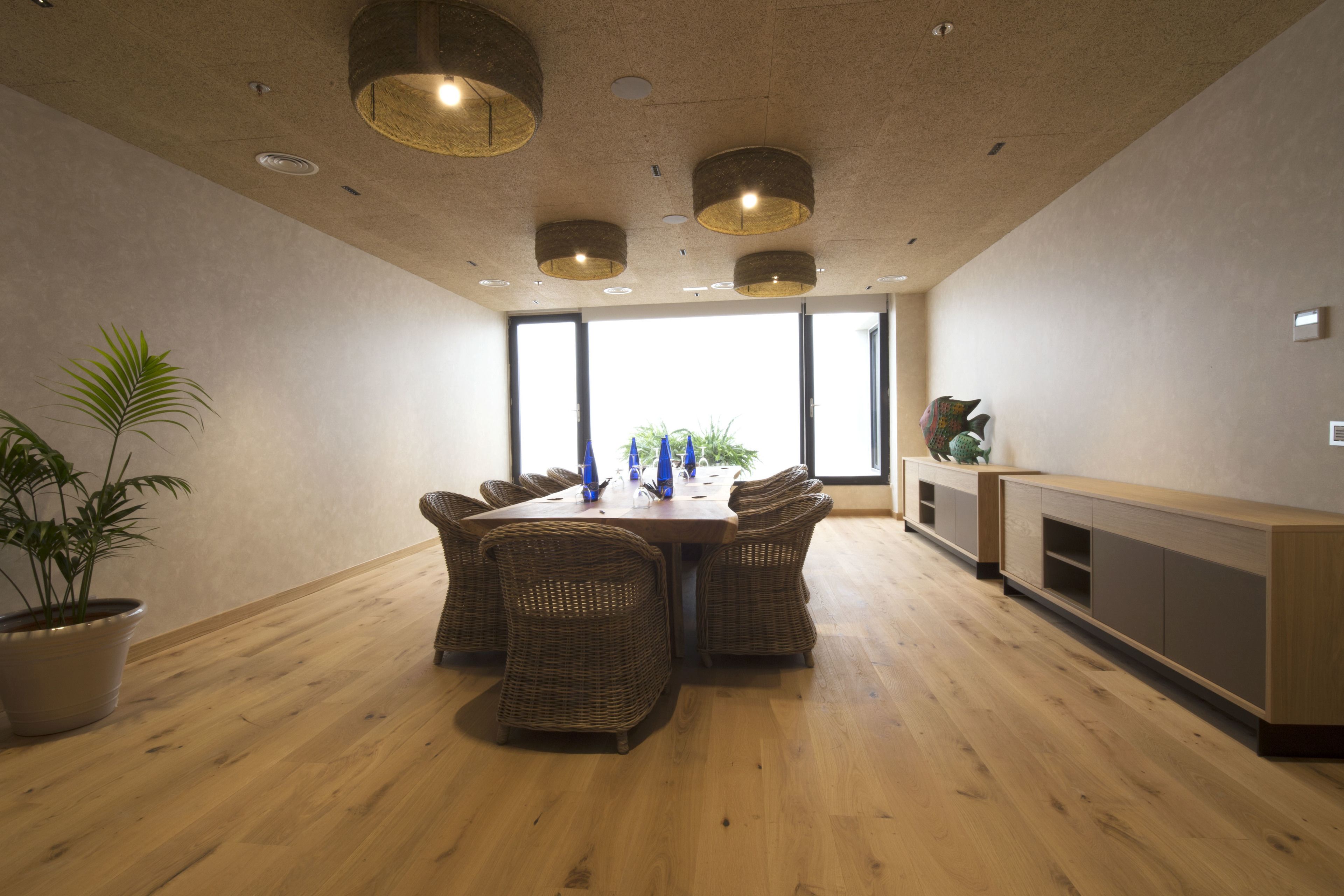 A modern dining area with a wooden table and wicker chairs, large windows, and a built-in wooden cabinet.