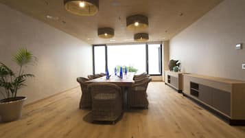 A modern dining area with a wooden table and wicker chairs, large windows, and a built-in wooden cabinet.