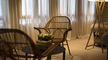Una habitación con una silla de mimbre, una mesita con una planta y una lámpara de pie.