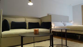 A modern hotel room with a sofa, a bedside table, and a lamp.