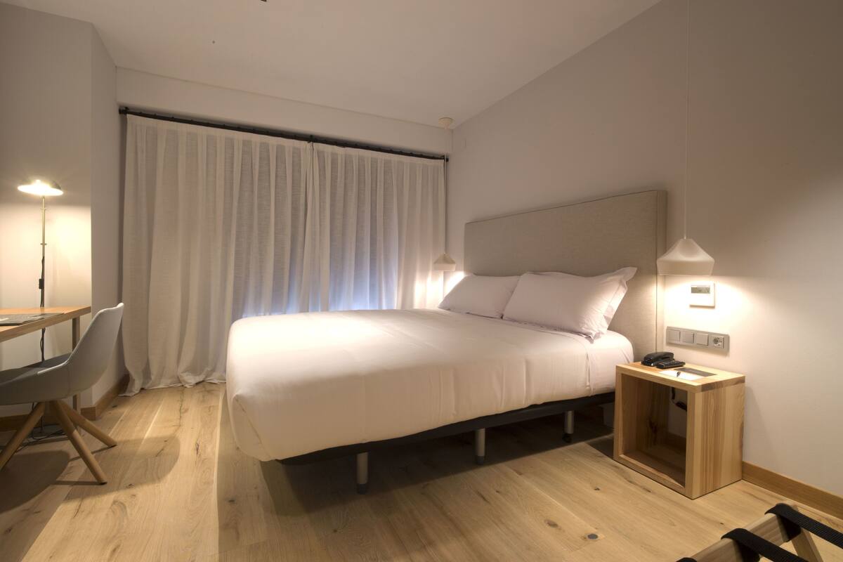 Une chambre d’hôtel moderne, dotée d’un grand lit, d’un bureau, d’une chaise et d’une table de chevet avec une lampe.